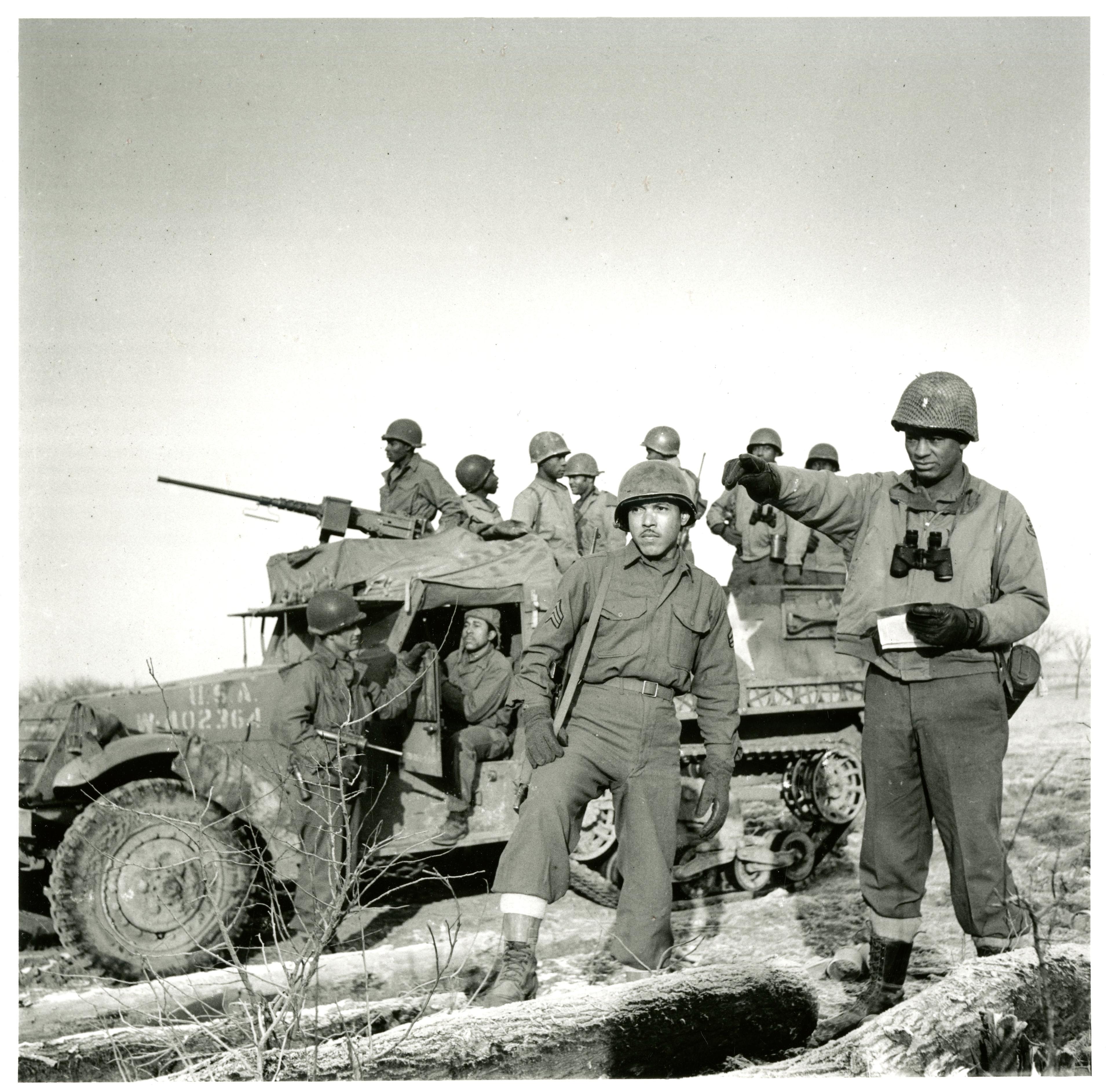 An image of a half-track of the 614th Tank Destroyer Battalion. In front of the half-track are two soldiers of the 614th TD Bn.