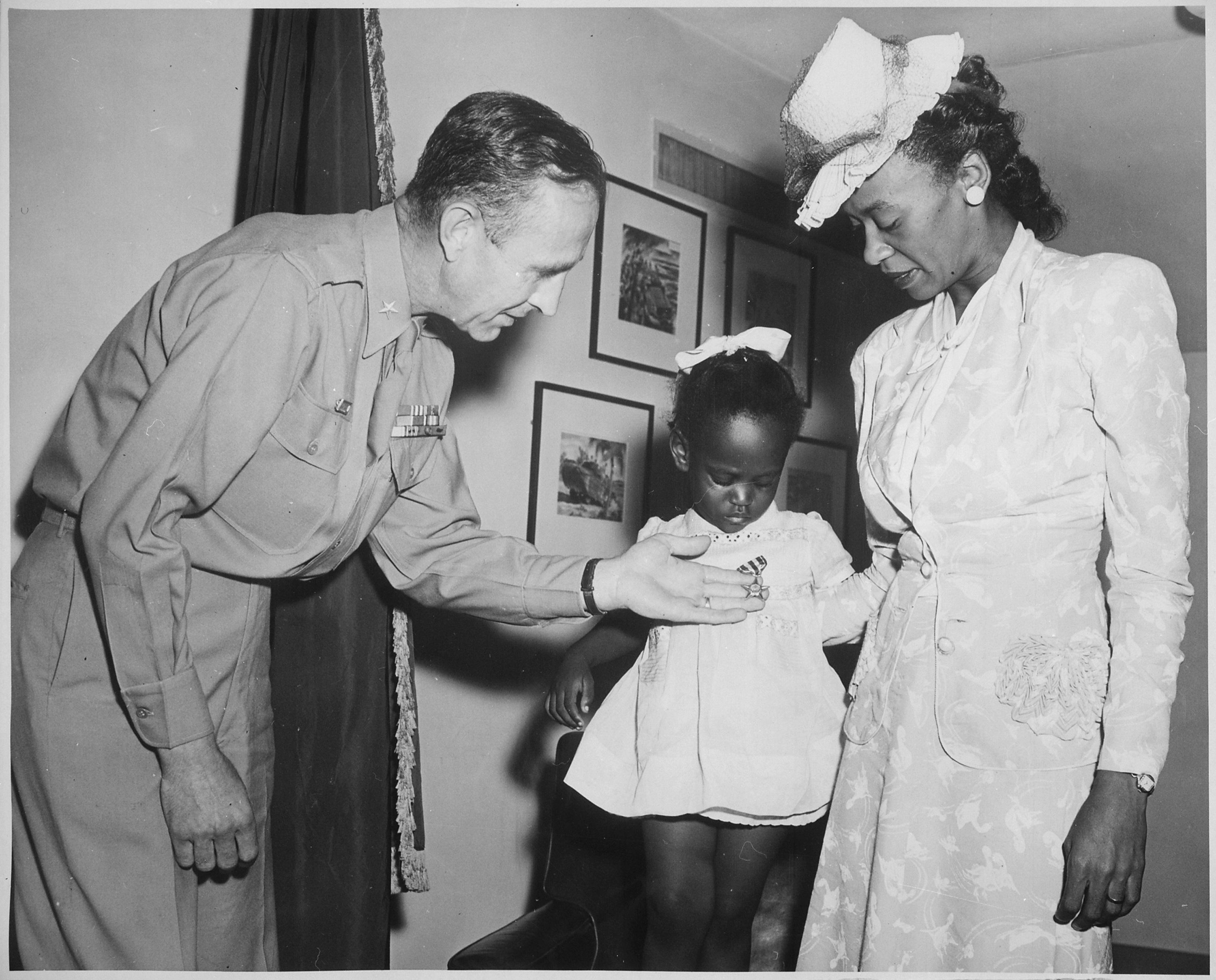  Brigade General Robert N. Young, Commanding General of the Military District of Washington, assists Melba Rose, aged 2, daughter of Mrs. Rosie L. Madison,...in viewing the Silver Star posthumously awarded her father 1st Lt. John W. Madison, of the 92nd Infantry Division, who was killed in action in Italy...