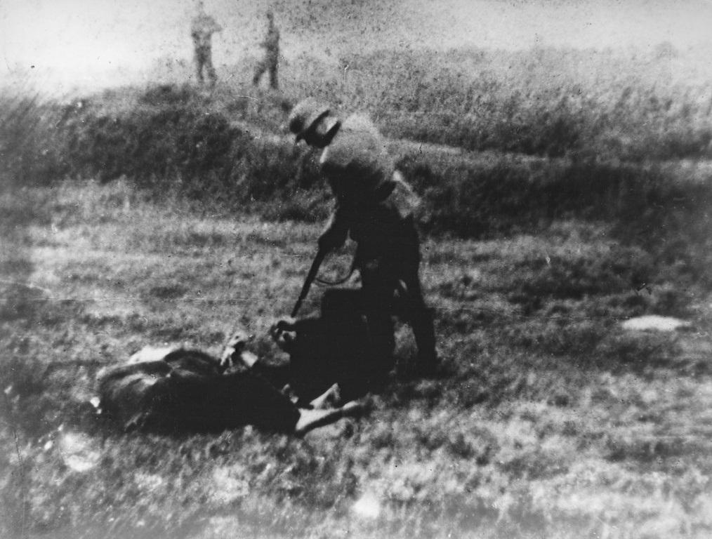 A German soldier points his rifle at a prisoner lying on the ground in the village Jajinci during World War II