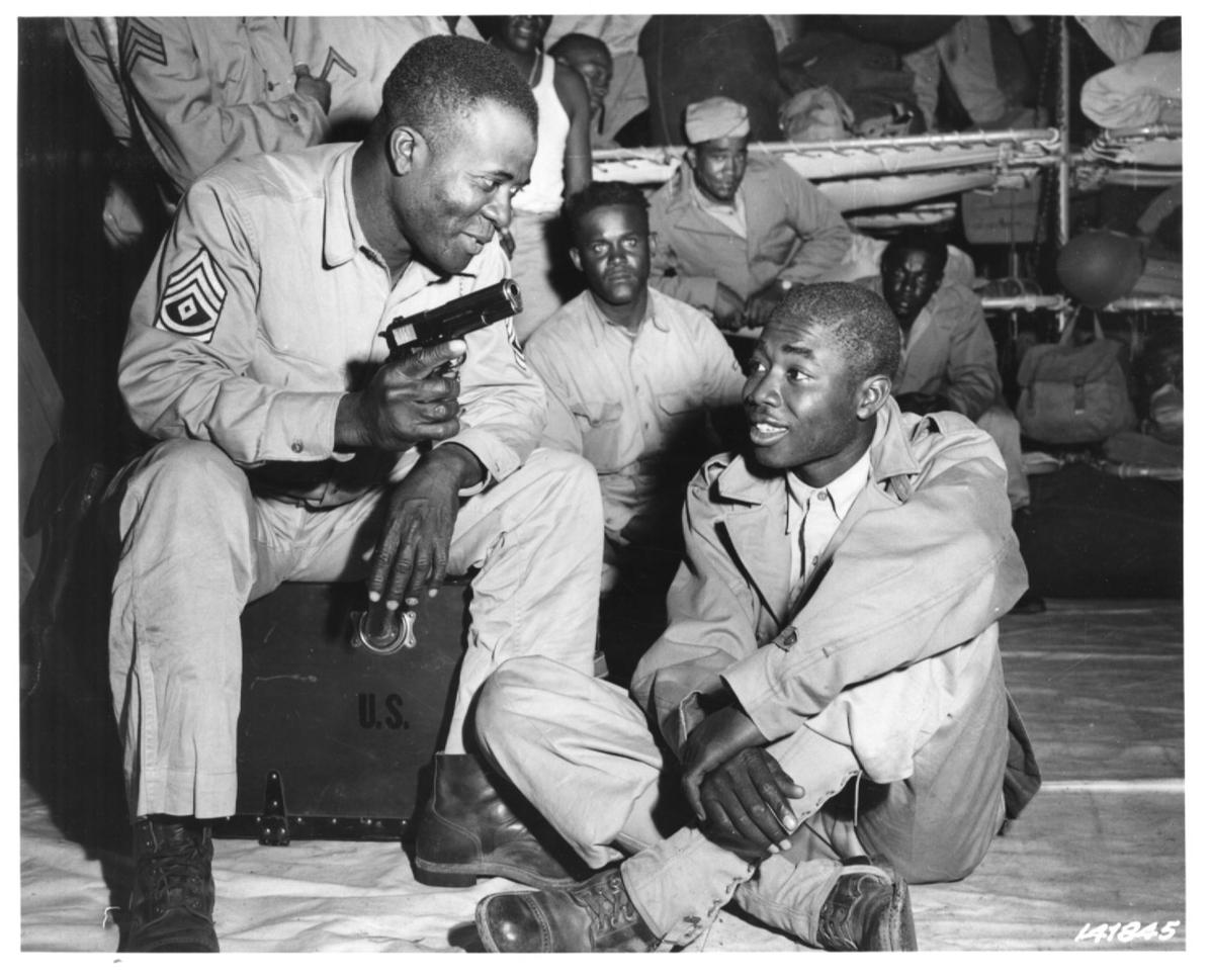 Historical image showing First Sergeant James Sims shows Private John Stephens his .45 pistol of Black American soldiers during WWII