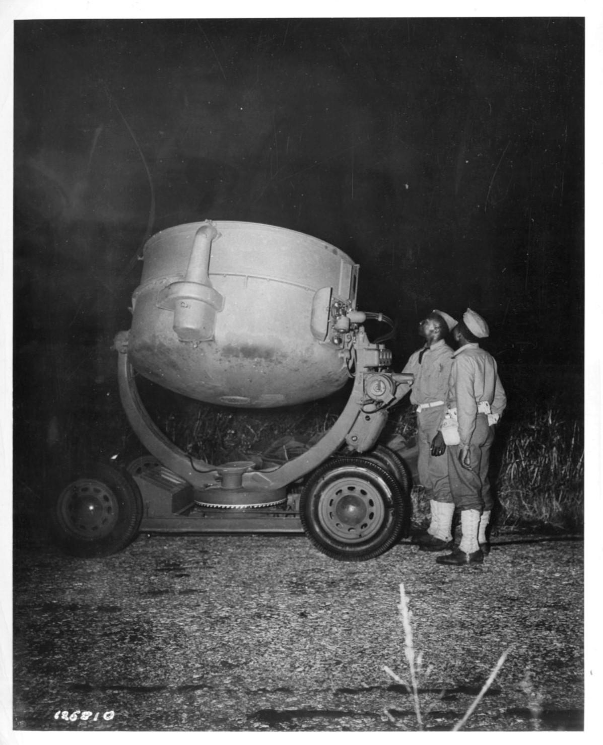 Historical image showing Soldiers of the 76th Coast Artillery Regiment stand next to a large searchlight of Black American soldiers during WWII