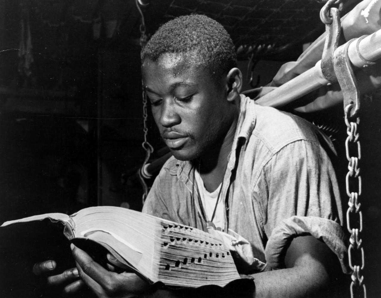 Historical image showing Steward's Mate Second Class James Lee Frazer reads the Bible of Black American soldiers during WWII