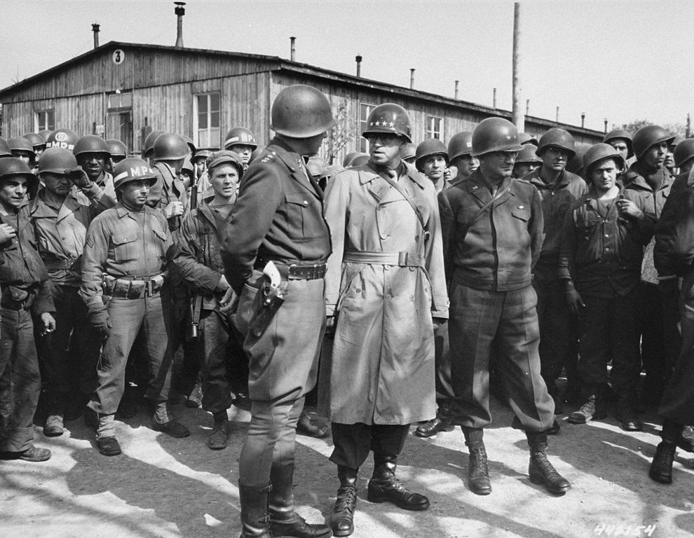 Historical image showing General George S. Patton converses with General Omar Bradly during their tour of the liberated Ohrdruf camp. On the left side, behind the MP, is a Black American soldier. of Black American soldiers during WWII