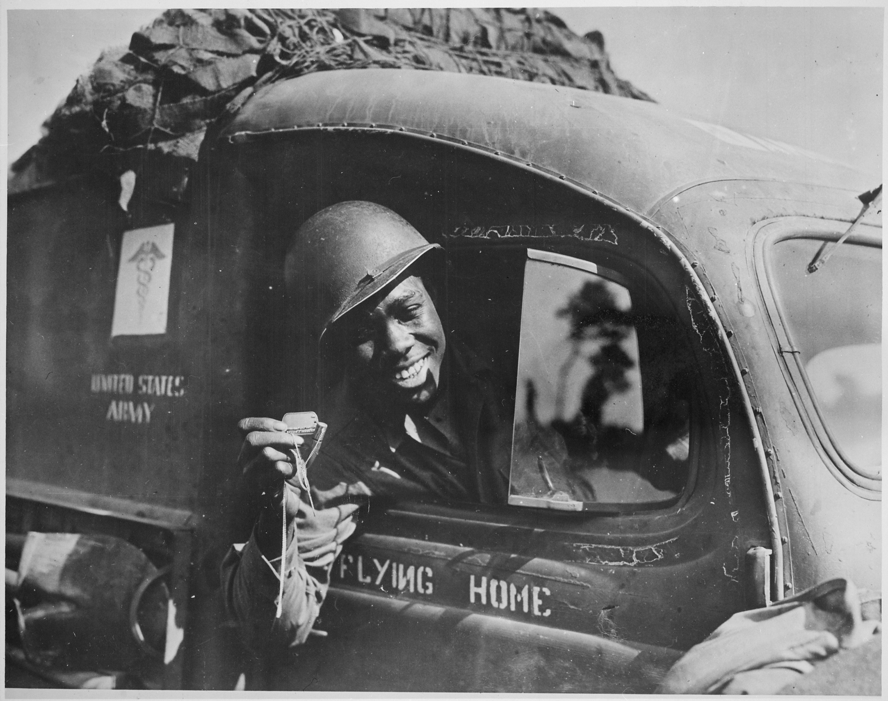 Historical image showing Private William A. Reynolds, an ambulance driver, shows a .50-caliber machine gun bullet which lodged above the windshield of his vehicle of Black American soldiers during WWII